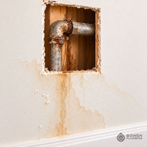 Corroded pipe leaking behind water-stained drywall, showing deterioration that may require whole-home repiping